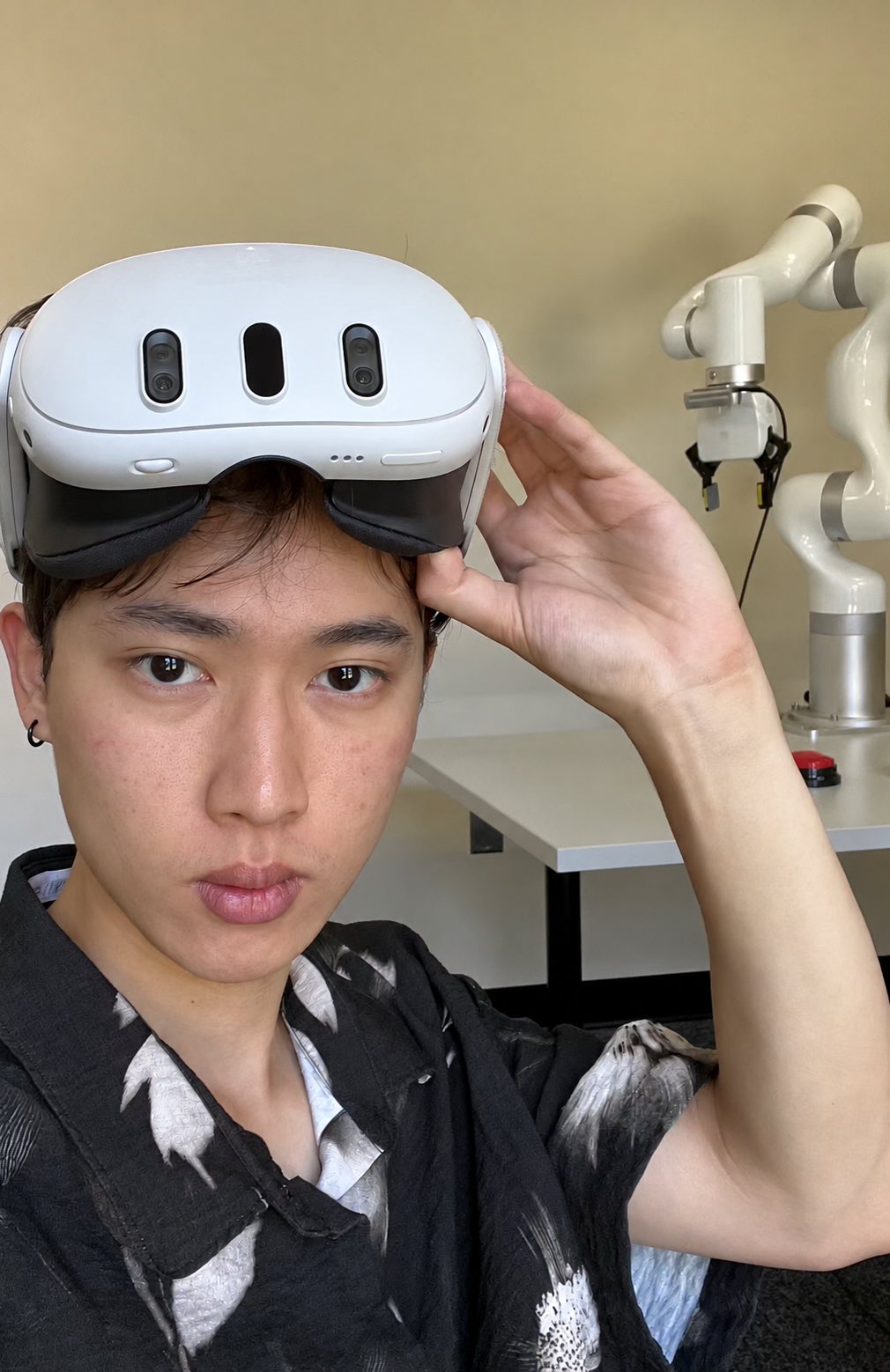 Kaixi Feng wearing a VR headset beside a robot arm in a robotics lab